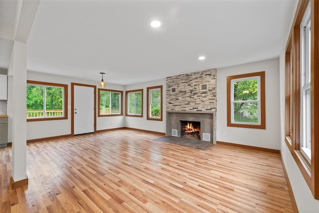 unfurnished living room with healthy amount of natural light, baseboards, a stone fireplace, and recessed lighting