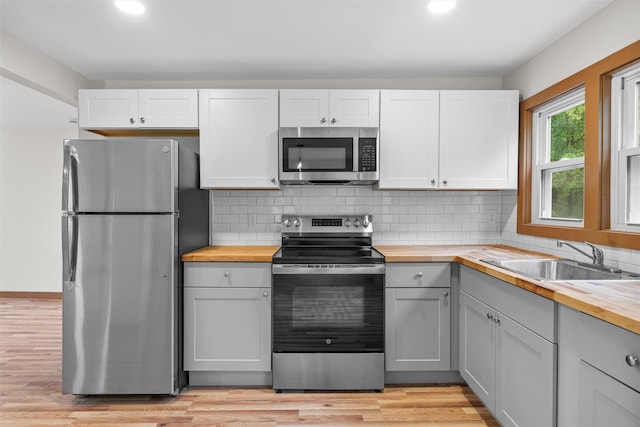 kitchen featuring appliances with stainless steel finishes, wooden counters, a sink, recessed lighting, and light wood-style floors