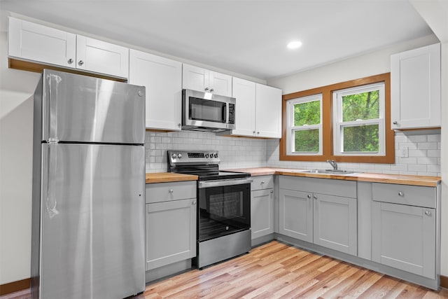 kitchen featuring stainless steel appliances, butcher block counters, a sink, gray cabinetry, and recessed lighting