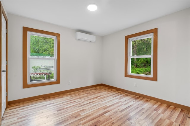 empty room with a wall mounted AC, plenty of natural light, light wood-style flooring, and baseboards