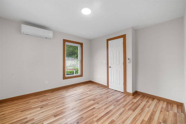spare room featuring a wall unit AC, light wood-type flooring, and baseboards