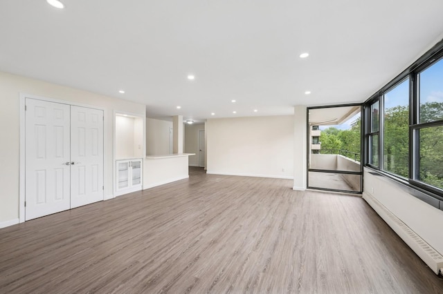 unfurnished living room with wood finished floors, baseboards, recessed lighting, and baseboard heating