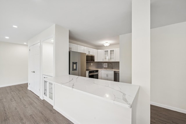 kitchen with stainless steel appliances, a sink, wood finished floors, white cabinetry, and light stone counters