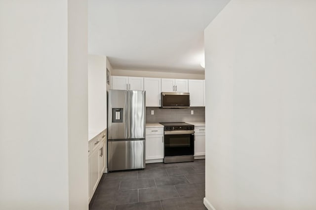 kitchen featuring stainless steel appliances, white cabinetry, light countertops, backsplash, and dark tile patterned flooring