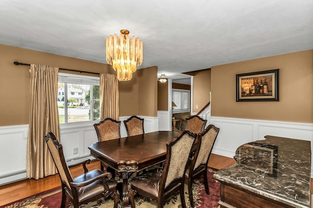 dining area with an inviting chandelier, a decorative wall, a baseboard heating unit, a wainscoted wall, and dark wood finished floors