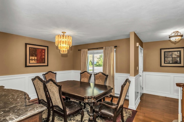 dining area featuring a decorative wall, an inviting chandelier, a wainscoted wall, and dark wood-type flooring