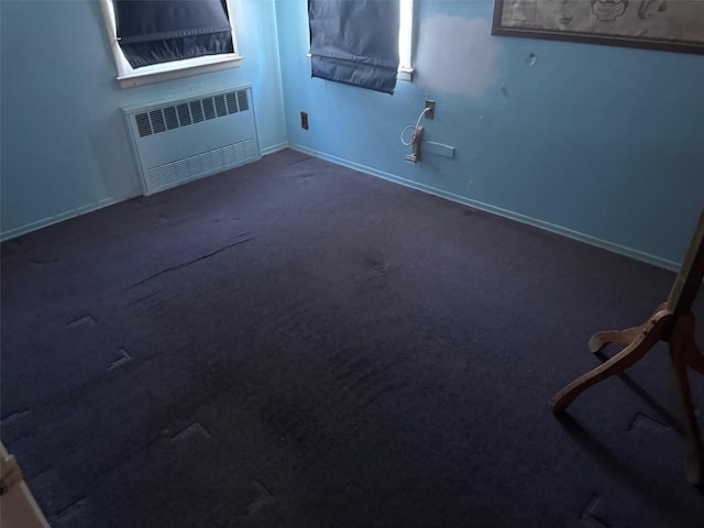 empty room with dark colored carpet, radiator, and baseboards
