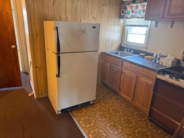 kitchen featuring range, dark countertops, wood walls, a sink, and freestanding refrigerator
