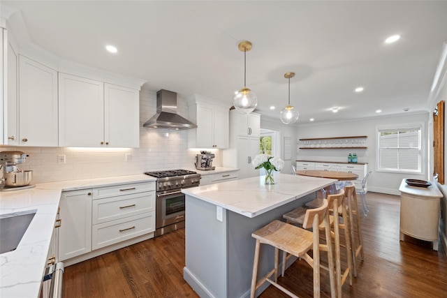 kitchen featuring wall chimney range hood, backsplash, dark wood-style flooring, stainless steel stove, and a breakfast bar