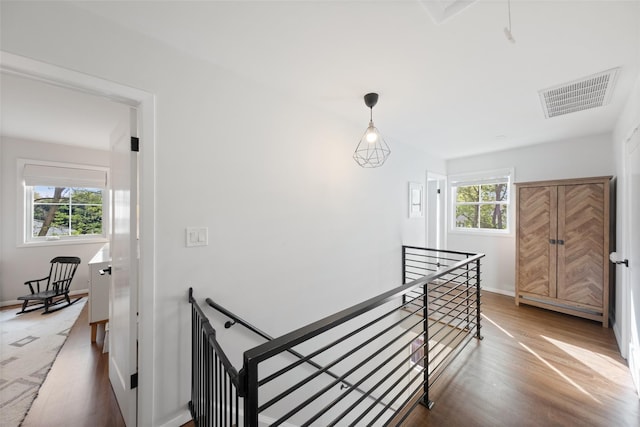 hallway with baseboards, an upstairs landing, wood finished floors, and visible vents