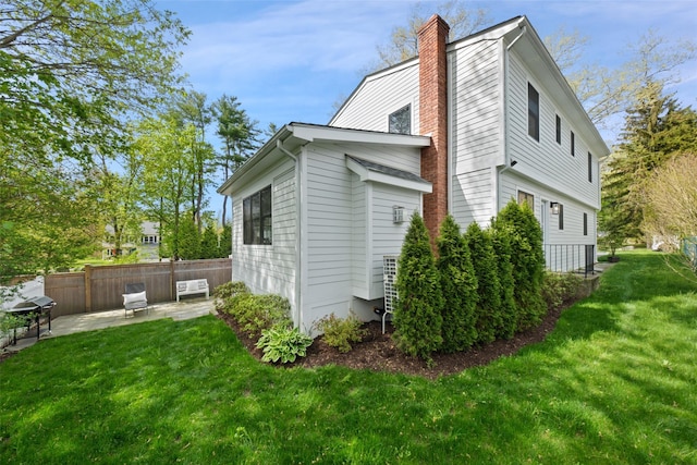 view of property exterior with a lawn, a patio, fence, and a chimney