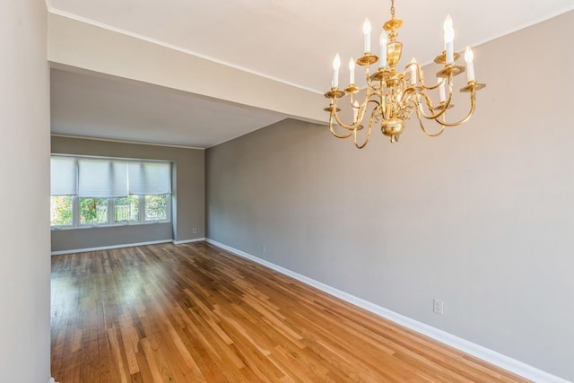 empty room featuring crown molding, baseboards, wood finished floors, and a notable chandelier