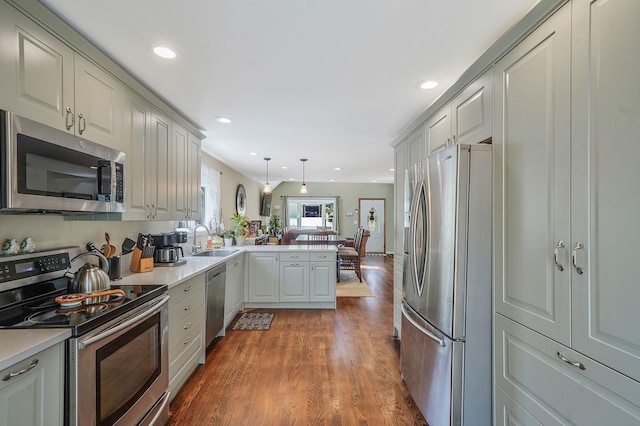 kitchen with dark wood-style flooring, a peninsula, light countertops, a sink, and appliances with stainless steel finishes