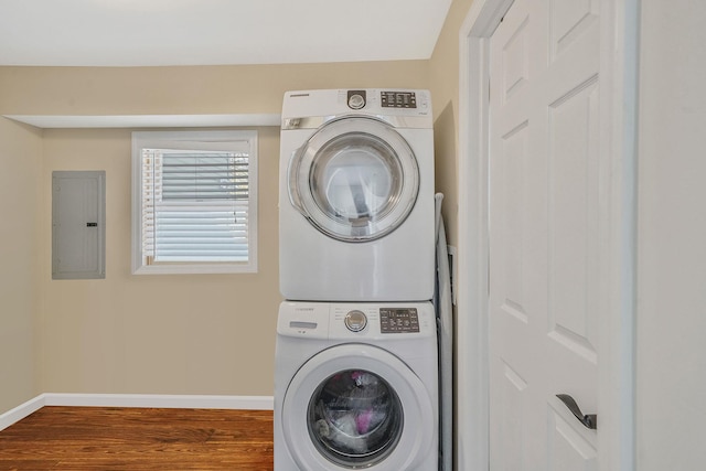 clothes washing area featuring baseboards, electric panel, stacked washer and dryer, and wood finished floors