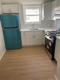 kitchen featuring freestanding refrigerator, range with gas stovetop, a sink, and light countertops