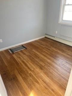 unfurnished room with baseboards, a baseboard heating unit, wood finished floors, and visible vents