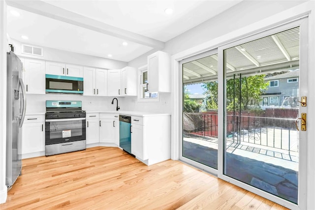 kitchen with white cabinets, a sink, light wood finished floors, light countertops, and stainless steel appliances