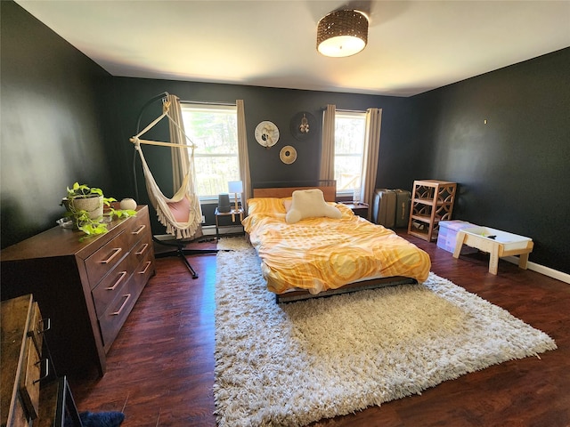 bedroom featuring dark wood-style flooring, baseboards, a baseboard heating unit, and multiple windows