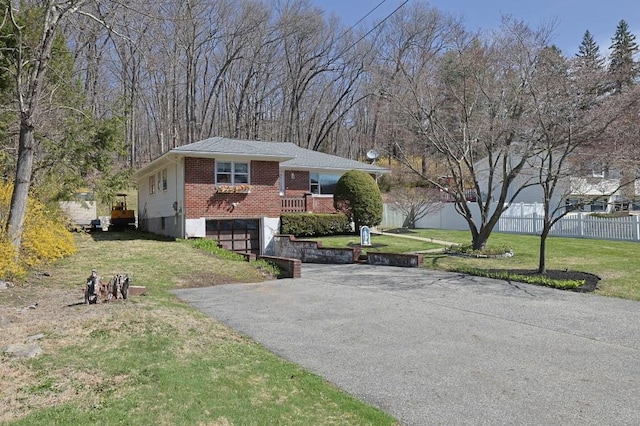 view of front facade featuring driveway, a front yard, brick siding, fence, and an attached garage