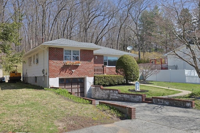 split level home featuring fence, a front lawn, brick siding, a garage, and driveway