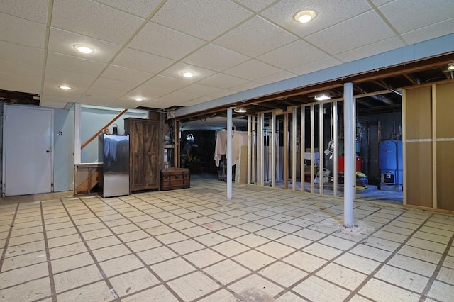 finished below grade area featuring a drop ceiling, fridge, and stairway