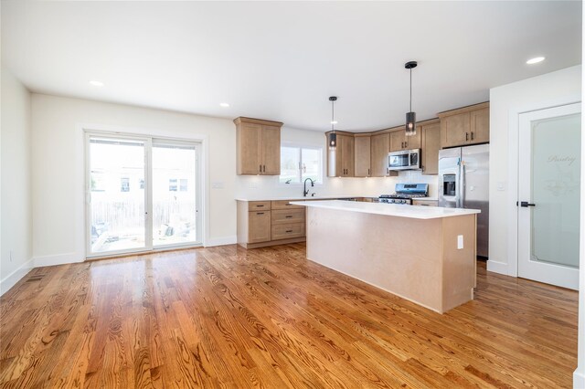 kitchen with light countertops, light wood finished floors, a kitchen island, and stainless steel appliances