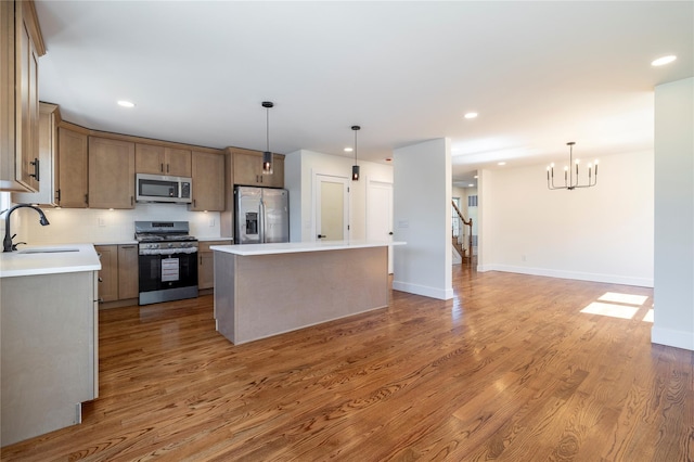 kitchen with a notable chandelier, a sink, light wood-style flooring, stainless steel appliances, and a kitchen island