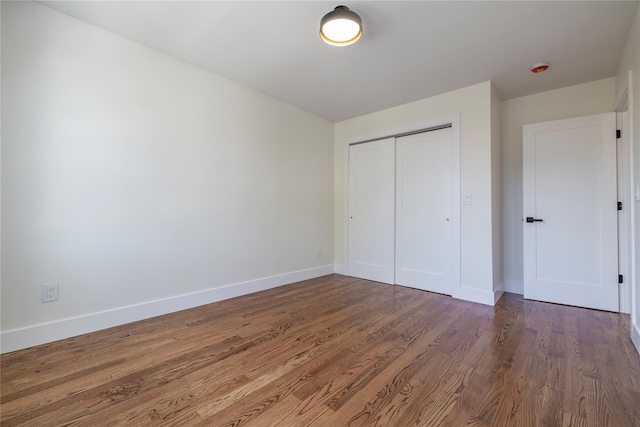 unfurnished bedroom with baseboards, wood finished floors, and a closet