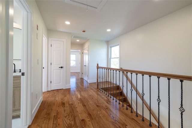corridor featuring baseboards, attic access, wood finished floors, and an upstairs landing