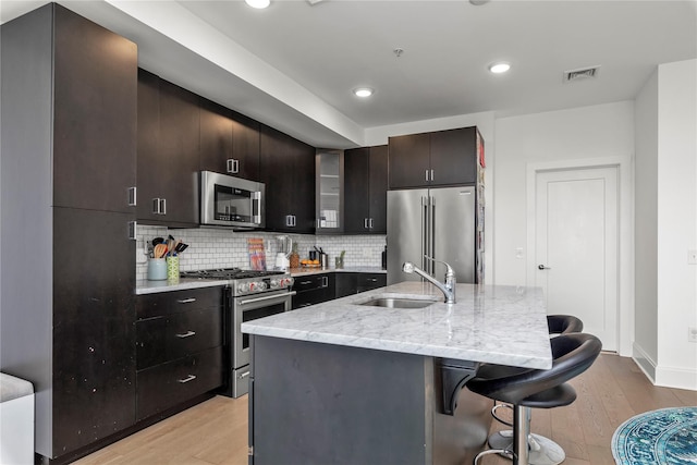 kitchen featuring a sink, high end appliances, light wood-style floors, and a kitchen bar