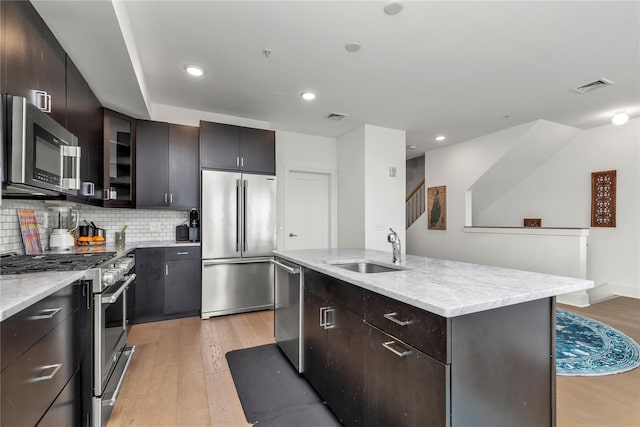kitchen with light stone countertops, appliances with stainless steel finishes, a sink, light wood-type flooring, and visible vents
