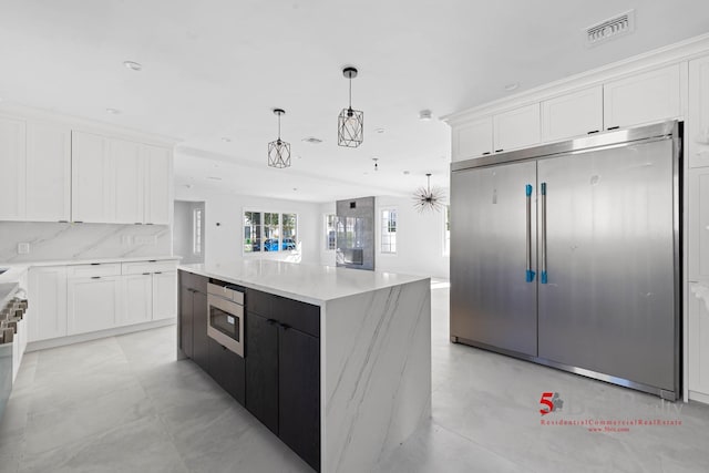 kitchen with white cabinets, built in appliances, a center island, decorative light fixtures, and visible vents