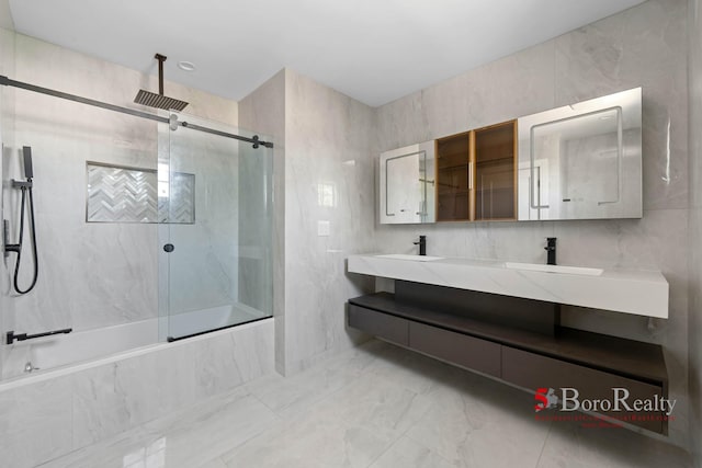 bathroom with a combined bath / shower with rainfall shower, double vanity, marble finish floor, tile walls, and a sink