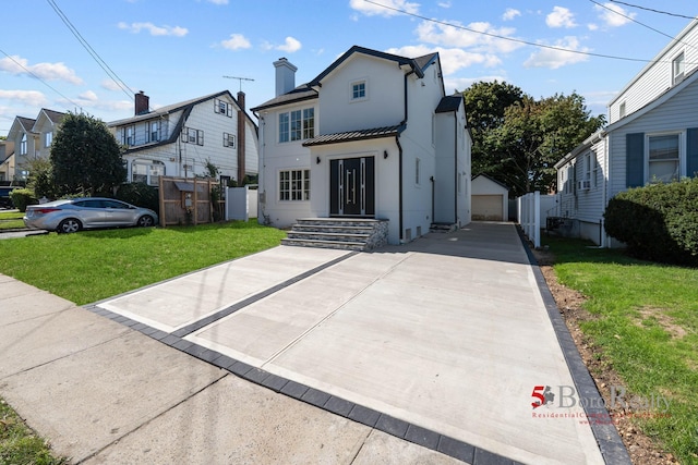 view of front of house with fence, a detached garage, stucco siding, a front yard, and an outbuilding