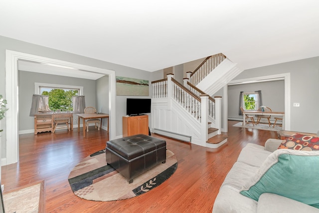 living room with a baseboard heating unit, a wealth of natural light, stairway, and wood finished floors