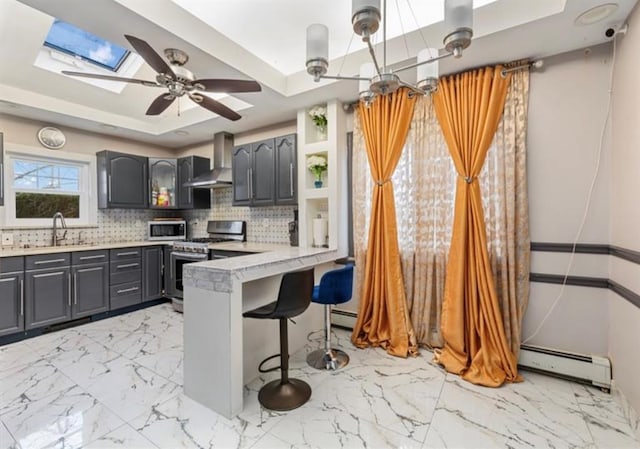 51 Graham St, Farmingdale, NY 11735 - kitchen featuring baseboard heating, wall chimney range hood, a tray ceiling, appliances with stainless steel finishes, and a skylight