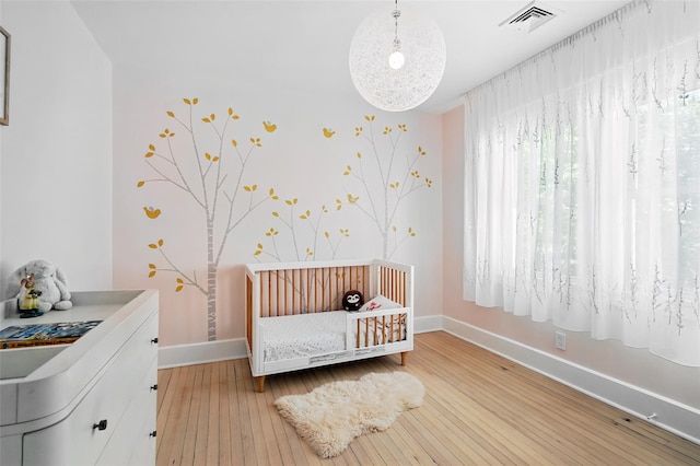 bedroom with baseboards, hardwood / wood-style floors, a nursery area, and wallpapered walls