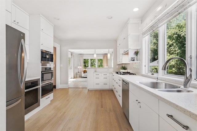 kitchen with appliances with stainless steel finishes, a sink, light wood-type flooring, white cabinetry, and open shelves