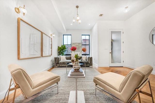 living area featuring baseboards, light wood-style flooring, a notable chandelier, and visible vents