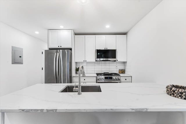 kitchen featuring electric panel, tasteful backsplash, light stone counters, a sink, and stainless steel appliances