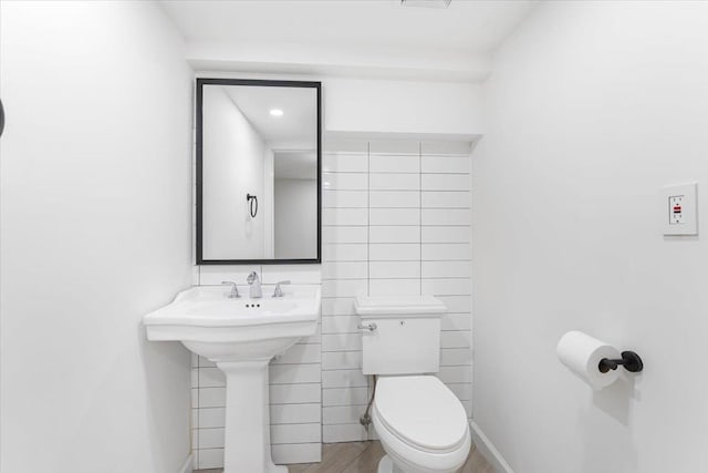 bathroom with toilet, tile walls, and a sink