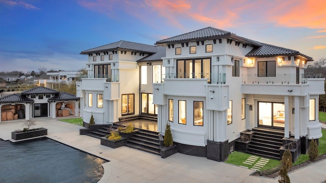 rear view of house featuring a patio, stucco siding, a balcony, and a tile roof