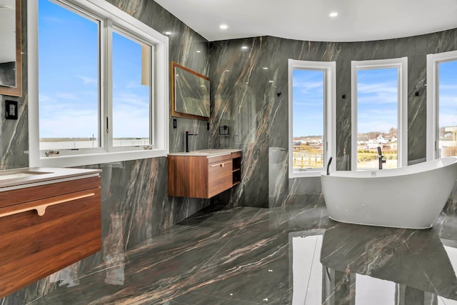full bath featuring vanity, marble finish floor, a freestanding tub, and a healthy amount of sunlight
