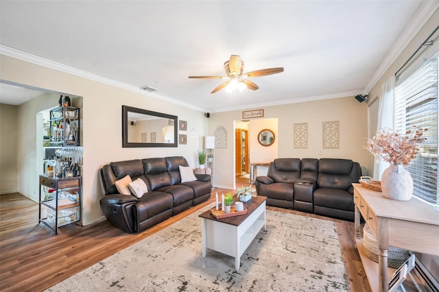 living room with a ceiling fan, visible vents, wood finished floors, baseboards, and ornamental molding