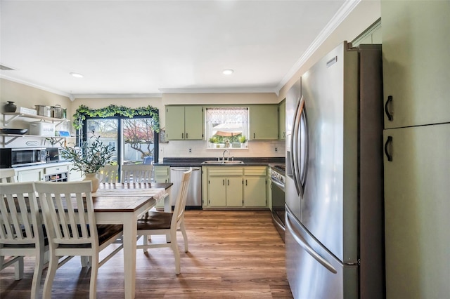 kitchen with dark countertops, green cabinetry, a sink, light wood finished floors, and stainless steel appliances