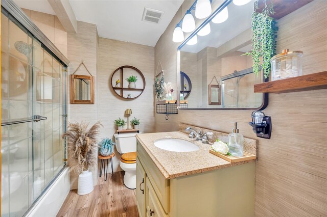 full bathroom with visible vents, wood finished floors, vanity, toilet, and enclosed tub / shower combo