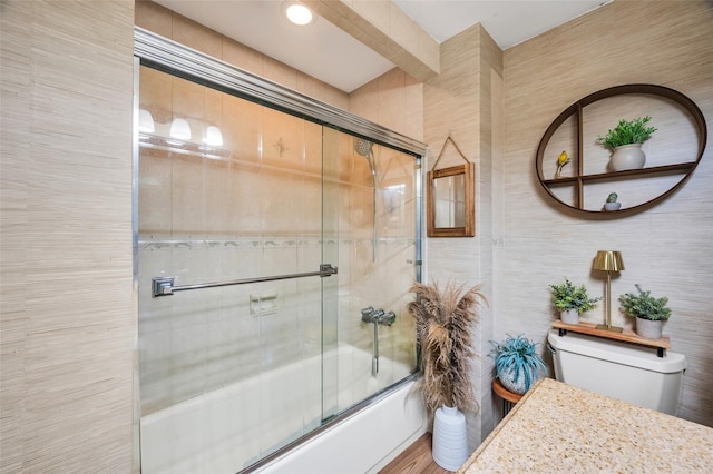 bathroom with shower / bath combination with glass door, wood finished floors, toilet, and tile walls