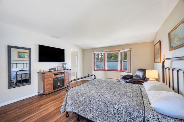 bedroom with a warm lit fireplace, baseboards, a baseboard radiator, and dark wood-type flooring