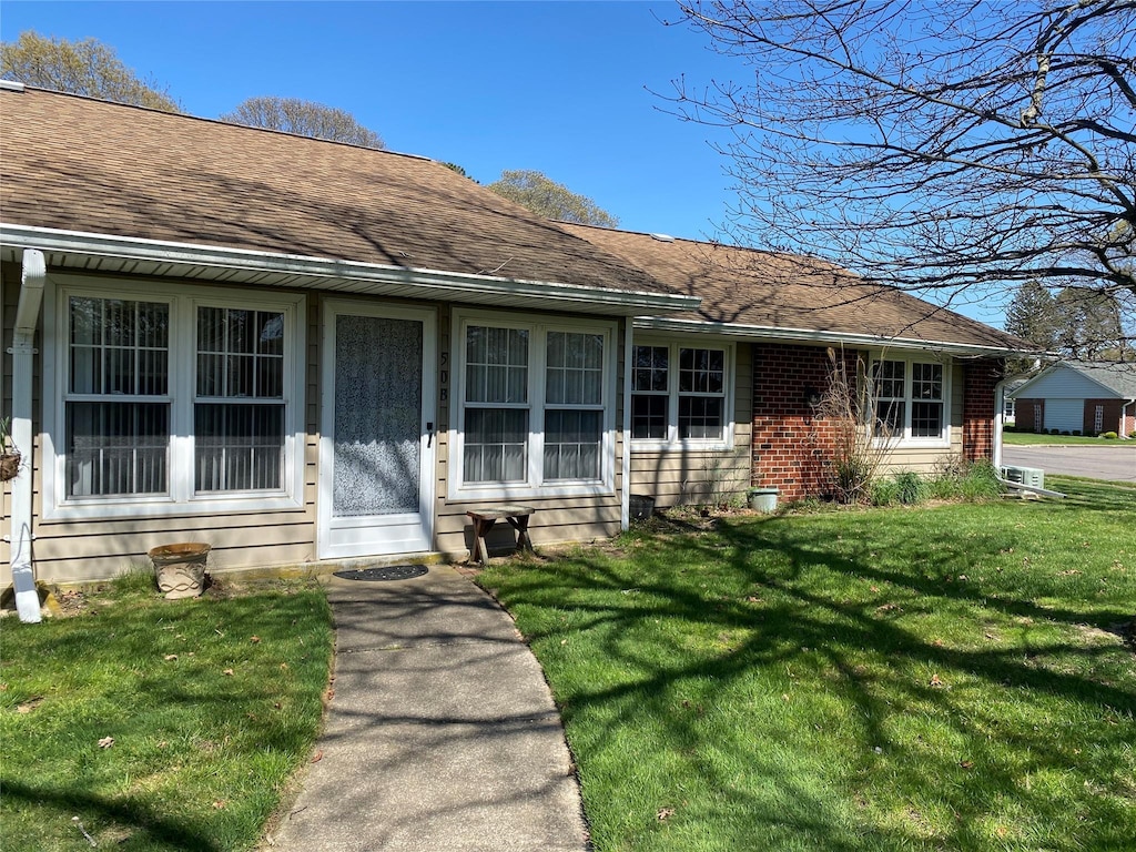 ranch-style house featuring roof with shingles, a front lawn, and brick siding