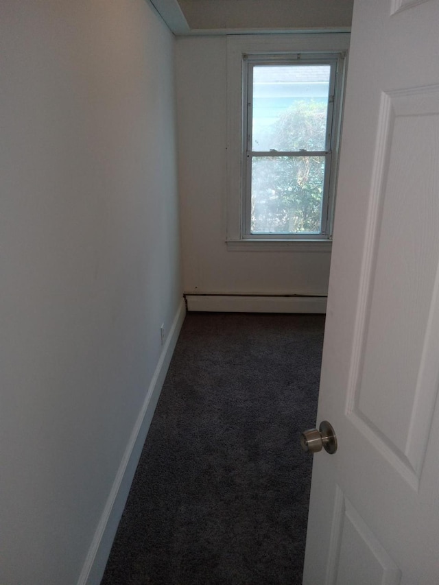 unfurnished room with dark carpet, baseboards, and a baseboard heating unit